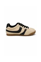 Zapatilla estilo urbano de gamuza color beige, con detalles en negro en los cordones, el talón y los laterales, y suela de goma marrón.