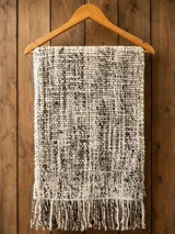 Pashmina tejida a mano en lana merino, con diseño melange en tonos crudo y marrón, y terminación de flecos en los extremos.