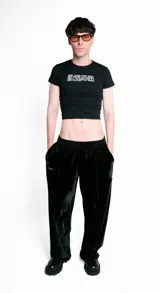 Pantalón de terciopelo negro de corte medio, con cintura elástica, dos bolsillos laterales, logo de la marca bordado en el frente y detalles de costuras delanteras. Es una prenda unisex.