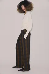Pantalón de tiro alto con diseño fluido y estampado de cuadros en tonos oscuros. Presenta pliegues frontales, bolsillos delanteros con solapa y cierre frontal con cremallera, botón y ganchos metálicos.