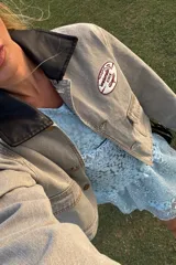 Campera de jean color visón con cuello desmontable de tela engomada negra. Presenta un bordado circular en el pecho y cierre frontal con botones metálicos.