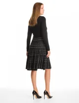 Vestido midi de punto con cuerpo liso negro de manga larga y falda acampanada con patrón geométrico vertical en contraste. Presenta escote redondo a la base y diseño entallado.