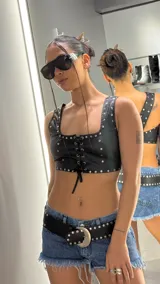 Top de cuerina negra sin mangas, con escote cuadrado, tirantes anchos y cierre frontal con cordones cruzados y tachas metálicas plateadas en los bordes.