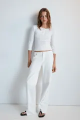 Jeans rectos de tiro medio en color blanco, con cinco bolsillos, trabillas y cierre frontal con cremallera. Presenta detalle de cordones cruzados con ojalillos metálicos a lo largo de los laterales de ambas piernas.
