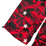 Pantalón de tiro bajo con estampado de camuflaje en tonos rojos y negros. Presenta diseño holgado, detalles de estrellas blancas aplicadas, paneles laterales con franjas verticales y bolsillos cargo.