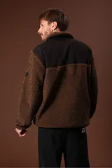 Cazadora de borreguillo color marrón, con cuello alto y cierre frontal parcial con cremallera. Presenta bolsillos laterales y diseño de manga larga.