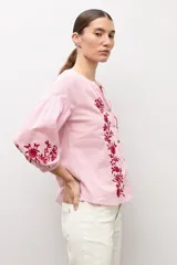 Blusa de manga larga con estampado de rayas verticales en tonos celestes y blancos. Presenta un escote en V con cierre frontal de botones y detalles de bordados florales en color crema en el frente y en los puños.