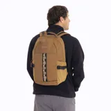 Mochila de 25 litros marca Merrell, modelo Trout Basic, en color mostaza. Confeccionada en poliéster Oxford con recubrimiento de poliuretano, presenta un compartimento principal con cierre, bolsillos laterales de malla con correas de compresión y una cinta frontal con bucles.