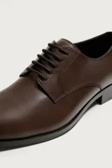 Zapato de vestir tipo derby en color negro, con diseño de parte superior lisa, horma redonda y suela con ligero tacón.
