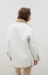 Campera acolchada de corte holgado, color blanco con diseño capitoneado en forma de rombos. Presenta cuello camisero y bordes internos con estampado floral en tonos azul y rojo, cierre frontal con botones a presión y bolsillos laterales.