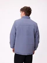 Campera reversible de nylon con cuello alto y cierre frontal. Un lado es de color gris liso con logo bordado, mientras que el otro lado presenta un estampado abstracto en tonos azules. Cuenta con bolsillos laterales y puños elásticos.