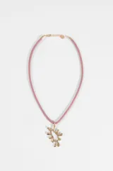 Collar corto con tira de cuero sintético rosado y dije colgante metálico con diseño texturizado irregular de sol. Cuenta con cierre de mosquetón y cadena de alargue dorada.