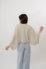 Blusa de lino color blanco, de diseño holgado, manga larga amplia acampanada con detalles de bordado en los puños y cuello redondo.