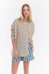 Camisa oversize de algodón con estampado de rayas multicolor en distintas direcciones, cuello camisero, mangas largas y detalle de botonera vertical en la espalda.