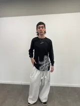Remera manga larga de algodón color negro, con diseño gráfico abstracto en tono gris en la parte inferior frontal y tipografía cursiva en la manga. Presenta cuello redondo reforzado y grifa de la marca en el puño.