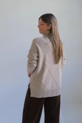 Polerón de cuello alto con diseño de rombos tejidos en relieve, mangas largas con puños acanalados y ruedo también acanalado.