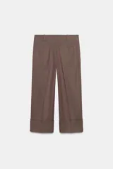 Pantalón marrón de tiro alto con bolsillos delanteros y traseros. El bajo está acabado con vuelta. Cierre frontal con cremallera y ganchos metálicos.