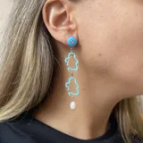 Aros colgantes con pasador y avíos metálicos plateados. Presentan un círculo naranja, una figura abstracta transparente con borde rosa, un círculo rosa con un strass y una pieza colgante naranja.