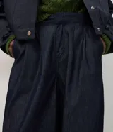 Pantalón de jean estilo aladín con cintura alta y pretina estructurada. Presenta pinzas frontales, volumen en la cadera y piernas con entalle progresivo que finalizan en puños con elástico, logrando un efecto jogger sofisticado.