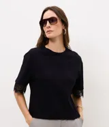 Remera negra de algodón, con cuello redondo, corte recto y mangas cortas amplias que presentan detalles de encaje en los puños.
