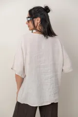 Blusa de lino color marrón oscuro, con escote redondo, mangas cortas amplias y detalle de alforzas verticales en el lateral derecho.