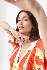 Vestido corto tejido calado a rayas horizontales en tonos naranja, amarillo y blanco, con cuello tipo polo y cierre frontal con botones.