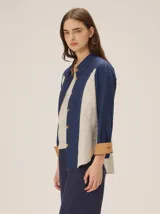 Camisa de lino color blanco con detalles combinados en tonos beige, cuello camisero, cierre frontal con botones oscuros y mangas largas con puños en contraste.