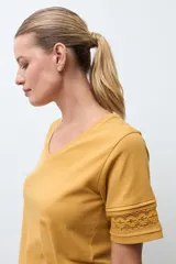 Remera blanca de algodón con cuello en V y mangas cortas que presentan un detalle de puntilla en los bordes.