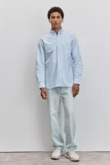 Camisa de manga larga en color celeste con estampado de rayas verticales finas, cuello abotonado y cierre frontal con botones.