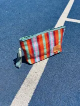 Sobre de mano rectangular con cierre superior y correa de muñeca, con diseño a rayas horizontales en tonos naranja, rojo, verde y celeste.
