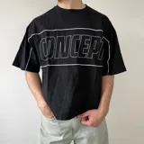 Remera negra de corte boxy, con mangas cortas y cuello redondo. Presenta un diseño estampado en el pecho con líneas blancas que enmarcan la palabra "CONCEPT" en tipografía grande y contorneada, además de ribetes blancos que recorren los hombros y las mangas.