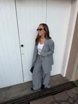 Conjunto de dos piezas compuesto por un blazer y un pantalón de corte sastrero, confeccionados en tela de algodón con estampado de rayas verticales blancas sobre fondo gris. El blazer presenta solapas clásicas y cierre frontal, mientras que el pantalón es de tiro medio y pierna recta.