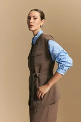 Chaleco negro de corte estructurado con cuello redondo, cierre frontal oculto y lazo ajustable en la cintura. Presenta dos bolsillos frontales con solapa y diseño de hombros caídos.