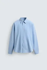 Camisa de algodón celeste con rayas verticales finas en blanco, de corte relajado (relaxed fit), cuello solapa y manga larga con puño abotonado.