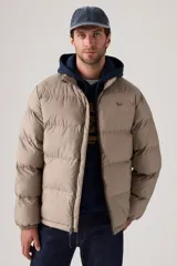 Campera puffer de corte corto y diseño acolchado horizontal, color beige. Cuenta con cierre frontal completo y logo de la marca en el pecho.