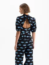 Top negro de jacquard con estampado de boquitas celestes. Presenta cuello con lazo, escote en V, mangas abullonadas con puños elásticos y un volado en el ruedo. Incluye recortes en el delantero y cierre trasero metálico.