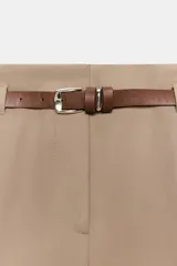Pantalón de vestir color beige, tiro alto, corte ancho y pierna recta. Presenta un bajo con vuelta y viene acompañado de un cinturón fino de cuero marrón con hebilla metálica.