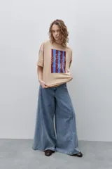 Remera blanca de calce relajado y silueta amplia, con cuello redondo, mangas cortas y estampa gráfica frontal de un cangrejo sobre franjas en tonos rosado y rojo.