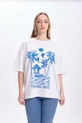 Remera blanca de corte amplio con estampado de palmeras, cabaña y aves en color azul.