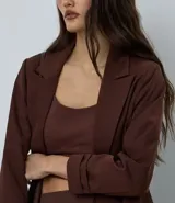 Blazer de sastrería color bordó, de corte oversized y largo, confeccionado en crepé. Presenta solapas clásicas, bolsillos frontales y detalle de pliegues en los puños.