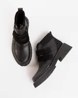 Bota corta de cuero vacuno color negro, con suela de caucho tipo tractor y cierre mediante doble tira de velcro en el empeine.