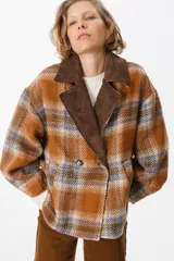 Blazer de corte holgado con diseño a cuadros en tonos naranja, azul y marrón. Presenta solapas anchas de pana en color marrón oscuro, cierre frontal cruzado con dos botones y bolsillos laterales integrados.