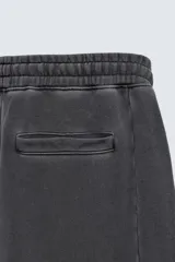 Pantalón jogger de corte wide fit confeccionado en tejido de algodón con interior de rizo. Presenta cintura elástica ajustable con cordón, bandas laterales decorativas, bolsillos laterales y un bolsillo trasero de plastrón. El acabado presenta un efecto lavado que le otorga una apariencia única.
