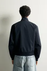 Cazadora relaxed fit de tejido ligero color azul marino, con cuello subido, manga larga y cierre frontal de cremallera. Cuenta con bolsillos frontales de vivo en la cadera y acabados en rib elástico en puños y cintura.
