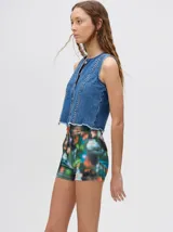 Chaleco de denim liviano con cierre frontal de botones metálicos, detalle de apliques metálicos verticales y ruedo con terminación desflecada.