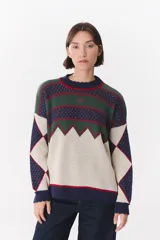 Buzo de tejido de punto con diseño geométrico y patrón de rombos, cuello redondo y mangas largas. Presenta una combinación de colores en azul marino, verde, beige y detalles en rojo.