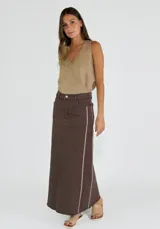 Pollera larga marrón oscuro, de corte recto, con talle alto y costura central vertical. Presenta un ribete contrastante de color beige claro a lo largo de los costados.