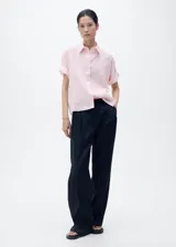 Camisa de manga corta color rosado, de diseño recto con cuello camisero y cierre frontal de botones.