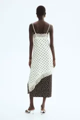 Vestido midi de satén blanco con estampado de lunares negros, escote en V con ribetes de encaje, breteles finos y bajo asimétrico con detalles de encaje.