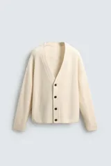 Cárdigan de punto color crema, con cuello pico, manga larga y cierre frontal de botones marrones. Presenta un calce relajado y acabados en rib.